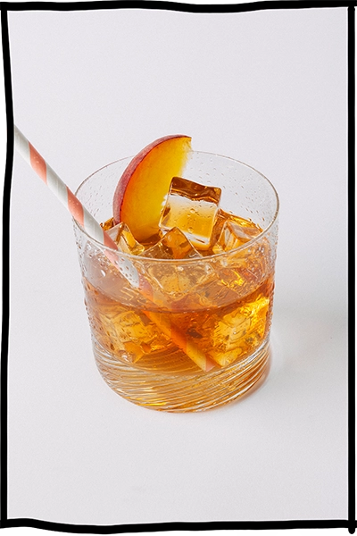 Ein Getränkeglas gefüllt mit Eistee von nosuga. Im Glas sind Eiswürfel, Pfirsichscheiben und ein Strohhalm.
