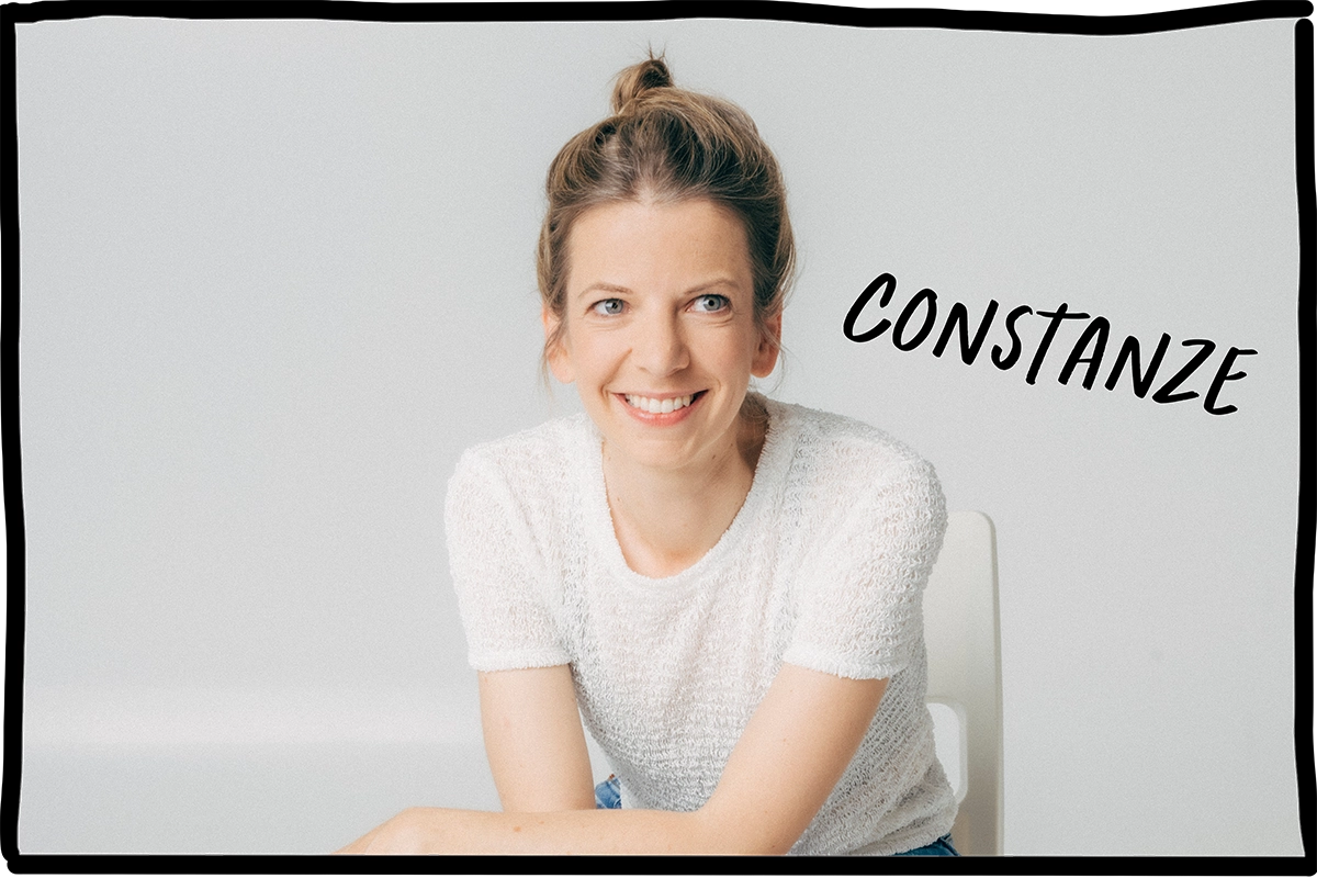 Eine Mitarbeiterin von nosuga sitz auf einem Stuhl vor weißem Hintergrund. Ihr Name steht auf dem Bild: Constanze.