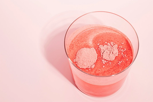 Ein Glas mit Wasser in dem ein pinkes Pulver hineingegeben wurde