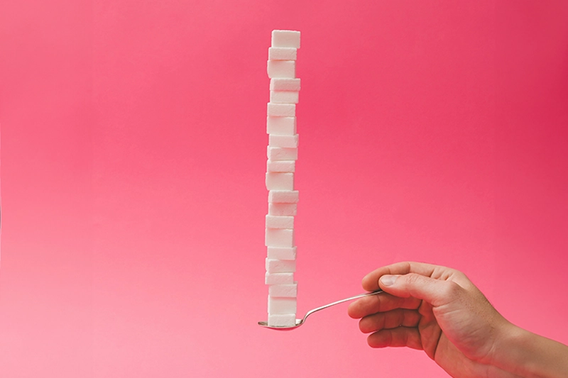 Eine Hand, die ein Löffel hält auf dem 21 Zuckerwürfel gestarpelt sind.